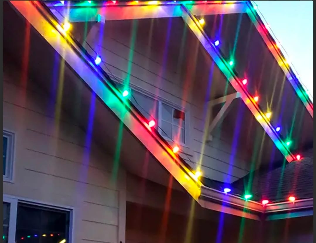 Close-up of multicolor C9 Christmas bulbs clipped along a home's gable eaves and gutter line