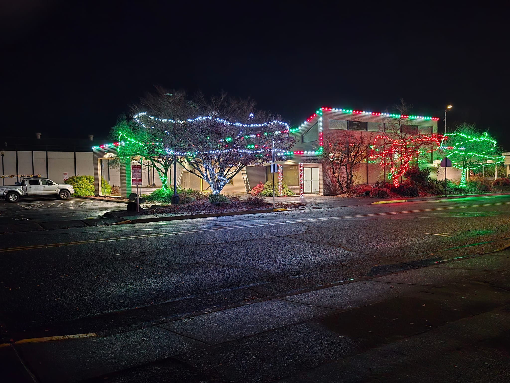 Commercial building with red, white and green C9 roofline lights and wrapped trees, a professional holiday lighting install