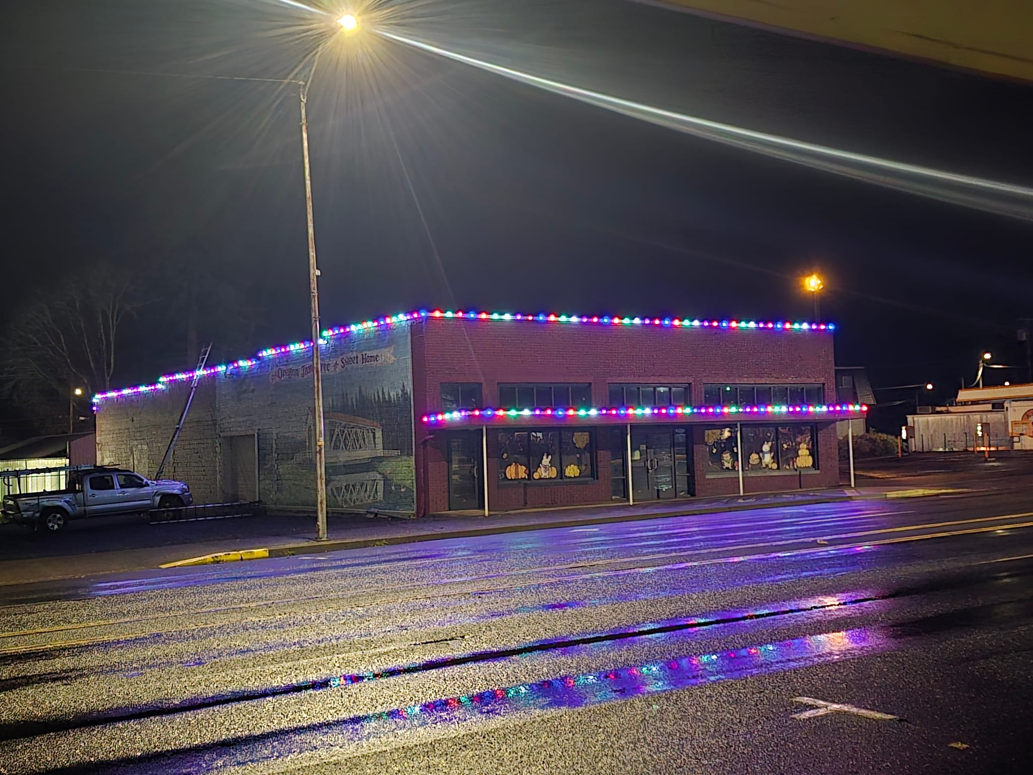 Multicolor C9 Christmas lights along the roofline and awning of a brick storefront in Sweet Home, Oregon, installed by On Top Home Services and affiliates