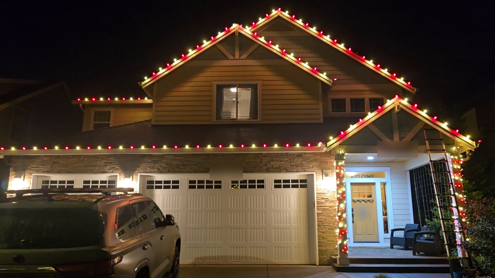 Two-storey home with red and warm white C9 Christmas lights on the rooflines and light-wrapped porch columns