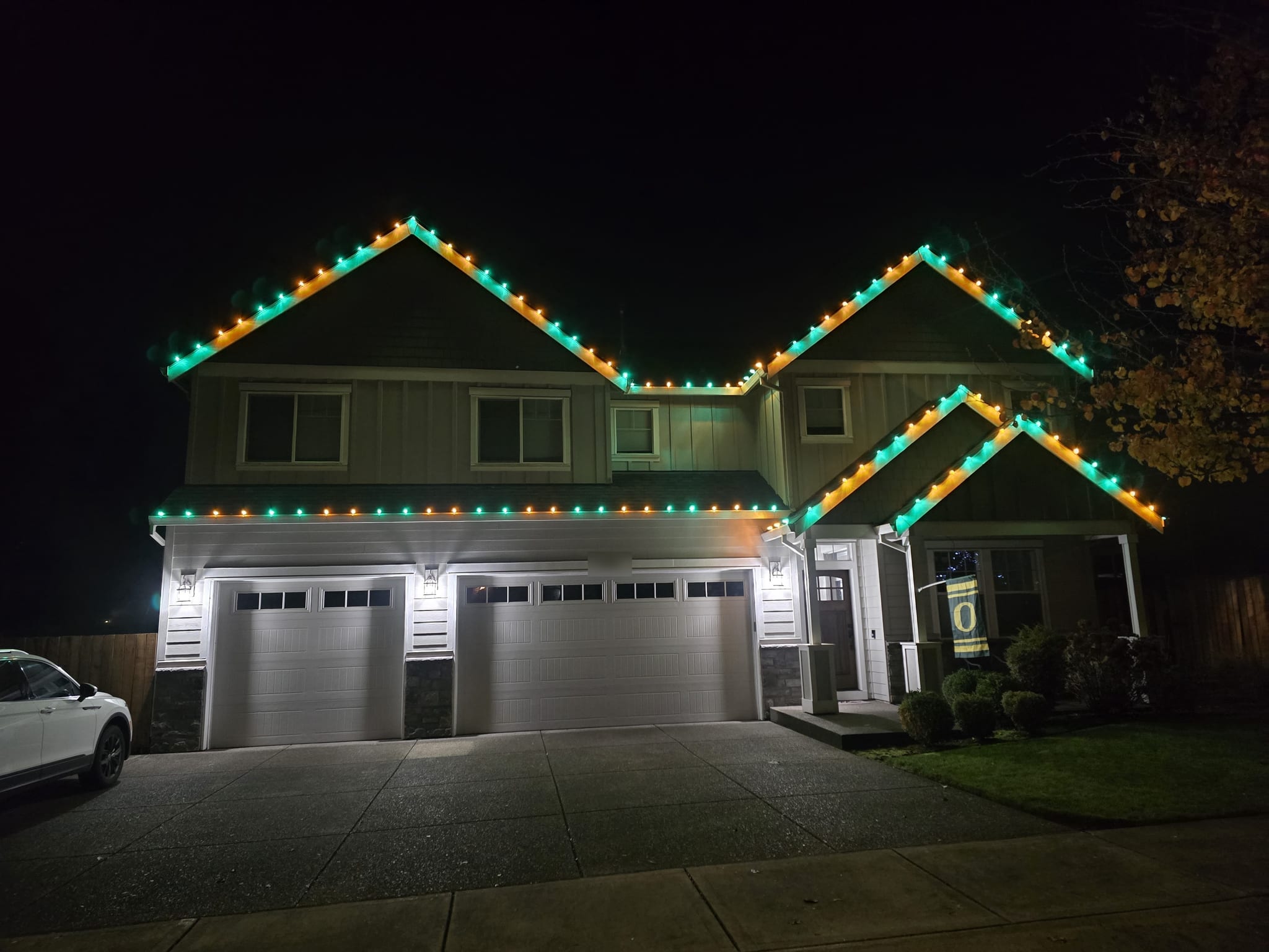 Two-storey home with teal and orange C9 Christmas lights outlining the gables and garage roofline