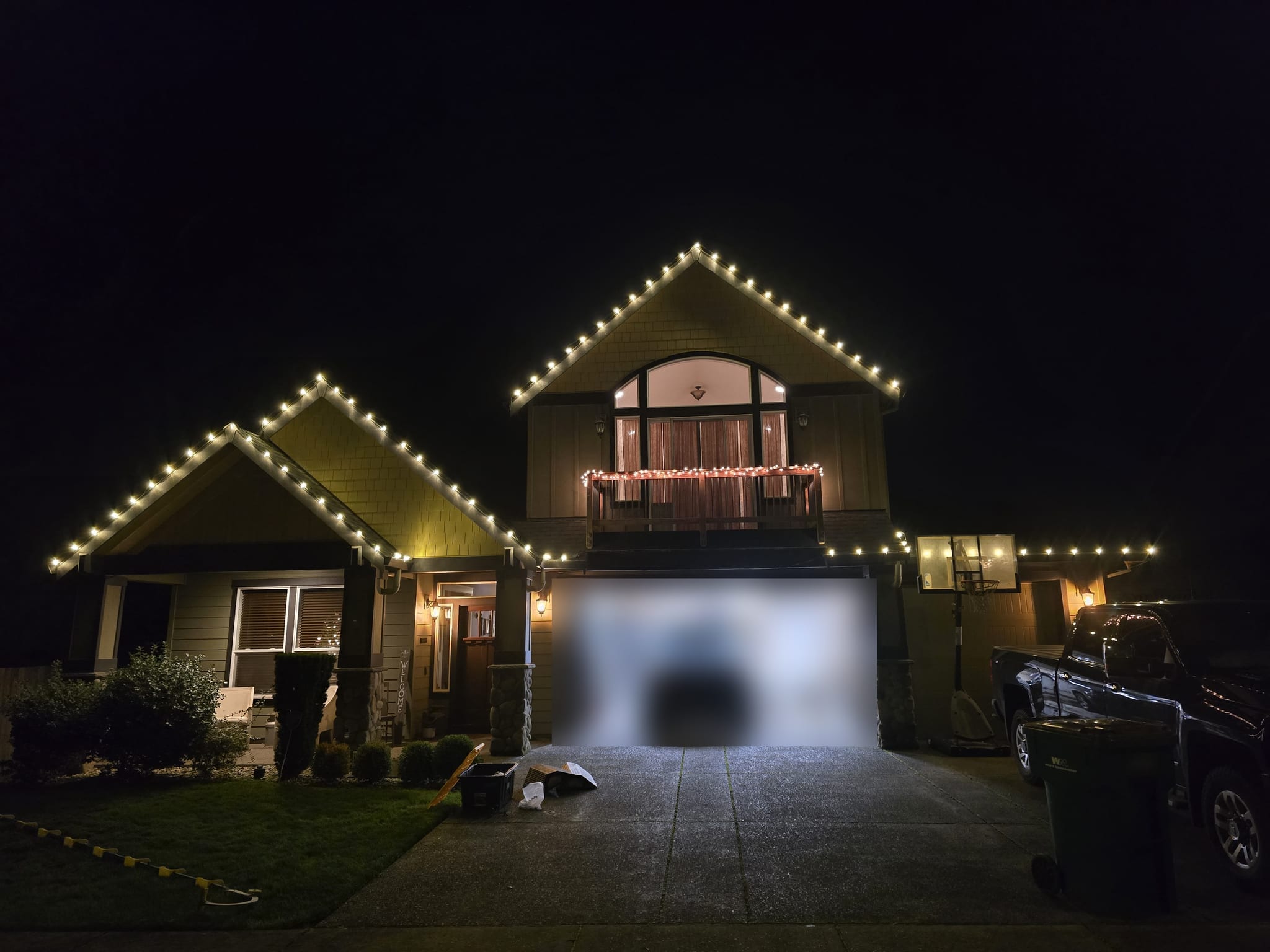 Craftsman-style home with warm white C9 Christmas lights along its gables and a lit balcony railing