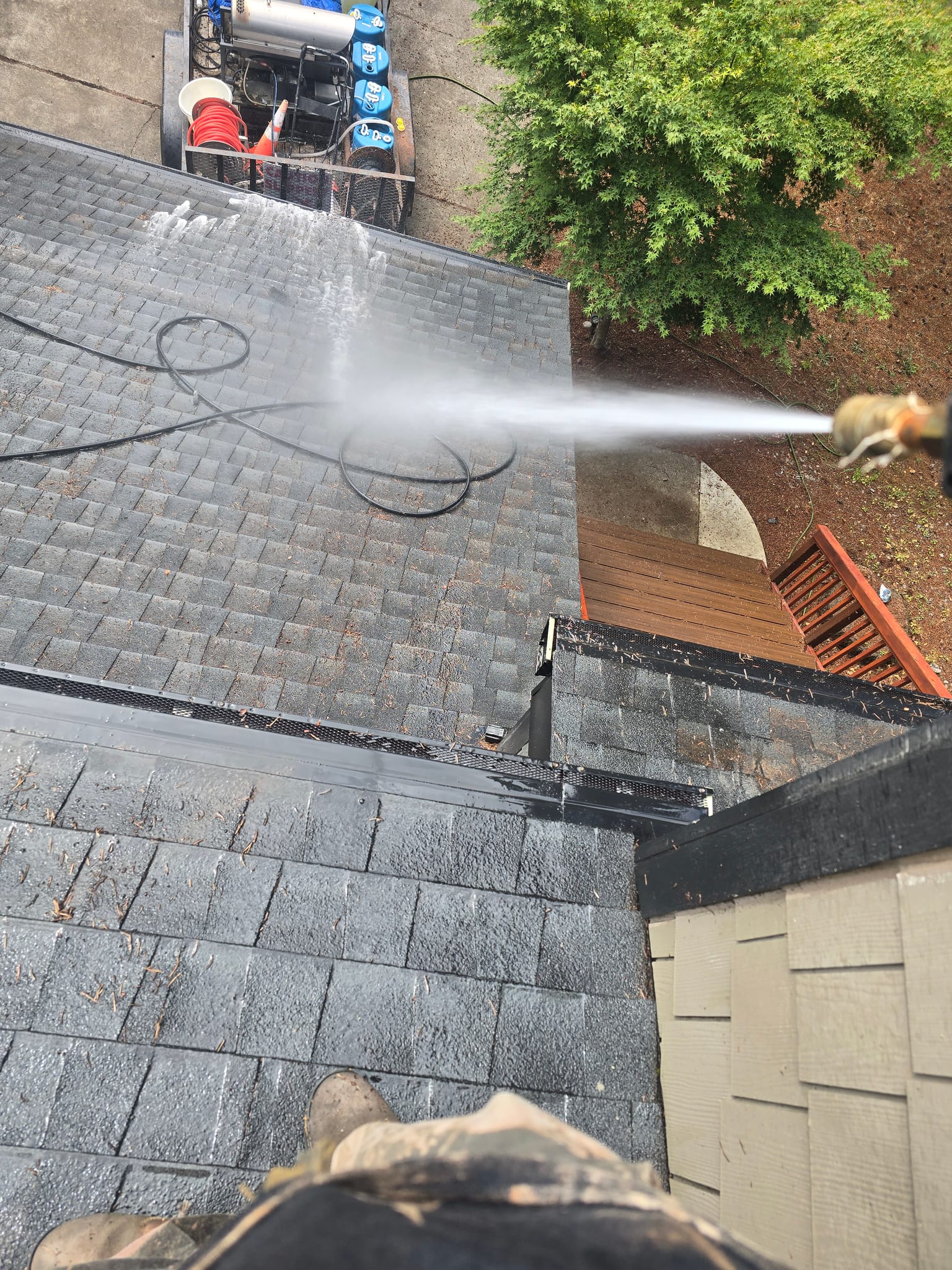 Soft-wash solution sprayed onto an asphalt roof, with the On Top Home Services wash trailer below