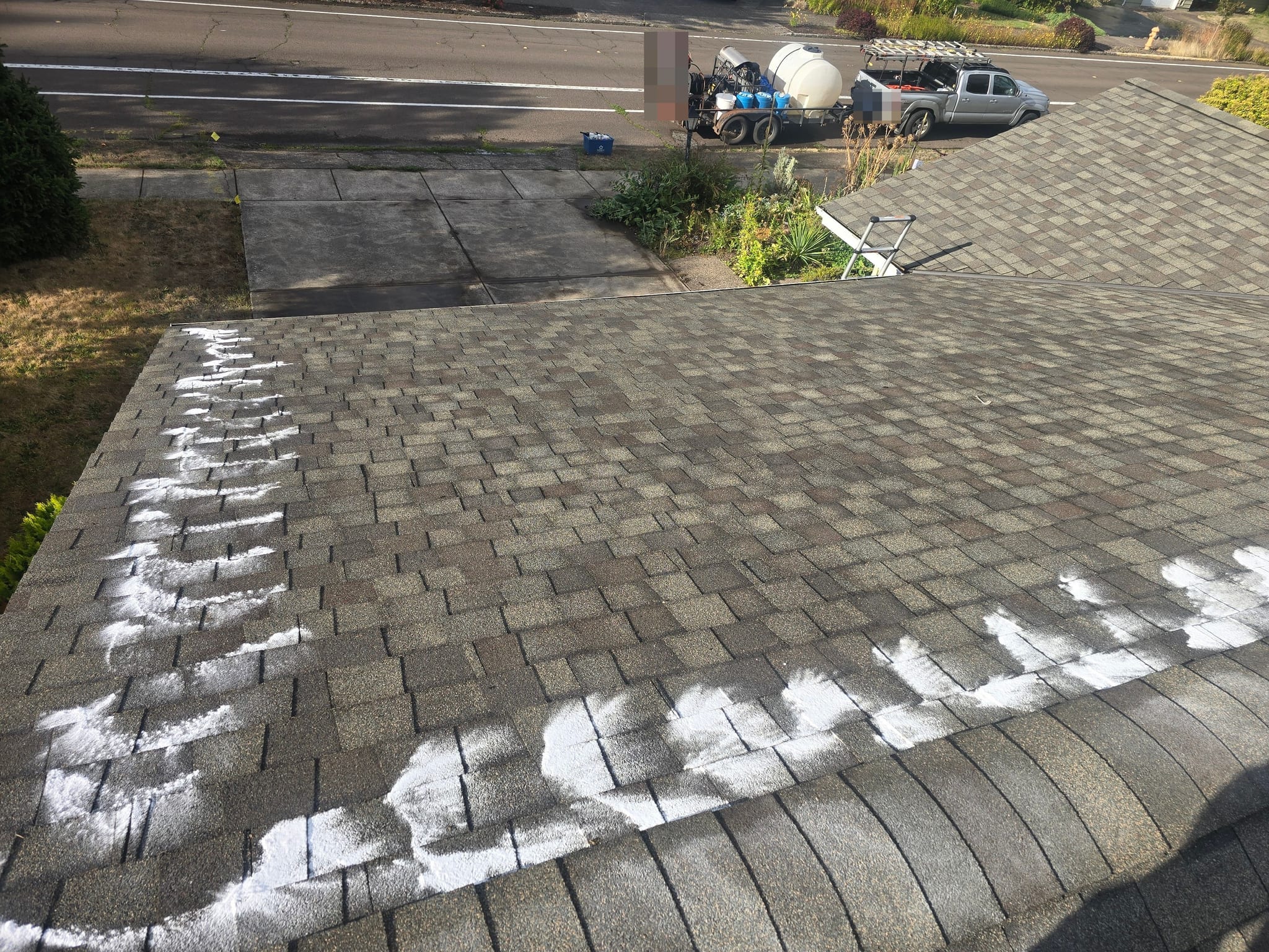 Soft-wash solution applied along the lower edge of an asphalt roof, with the wash truck and trailer parked on the street